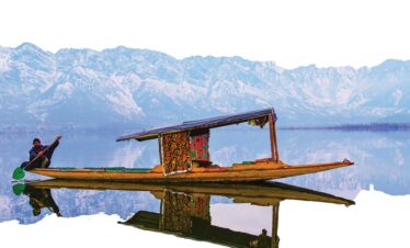 Traditional Shikara boat on Dal Lake with snow-covered Himalayas in the background, Kashmir, India